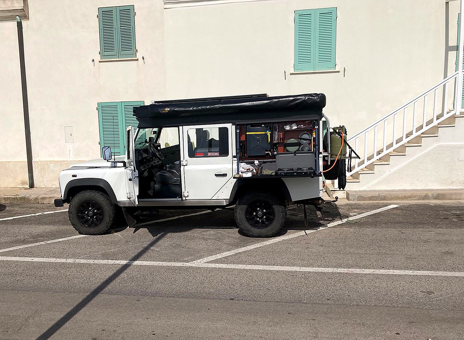 Land Rover Defender 110 on the road with the side storage box folded open as a cooking box