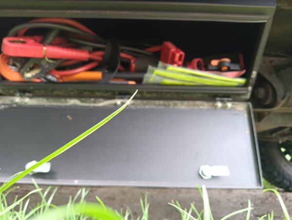Chassis storage box in gebruik gevuld Geöffnete chassis storage box gefüllt mit Starthilfekabeln und Bergungsausrüstung unter einem Defender