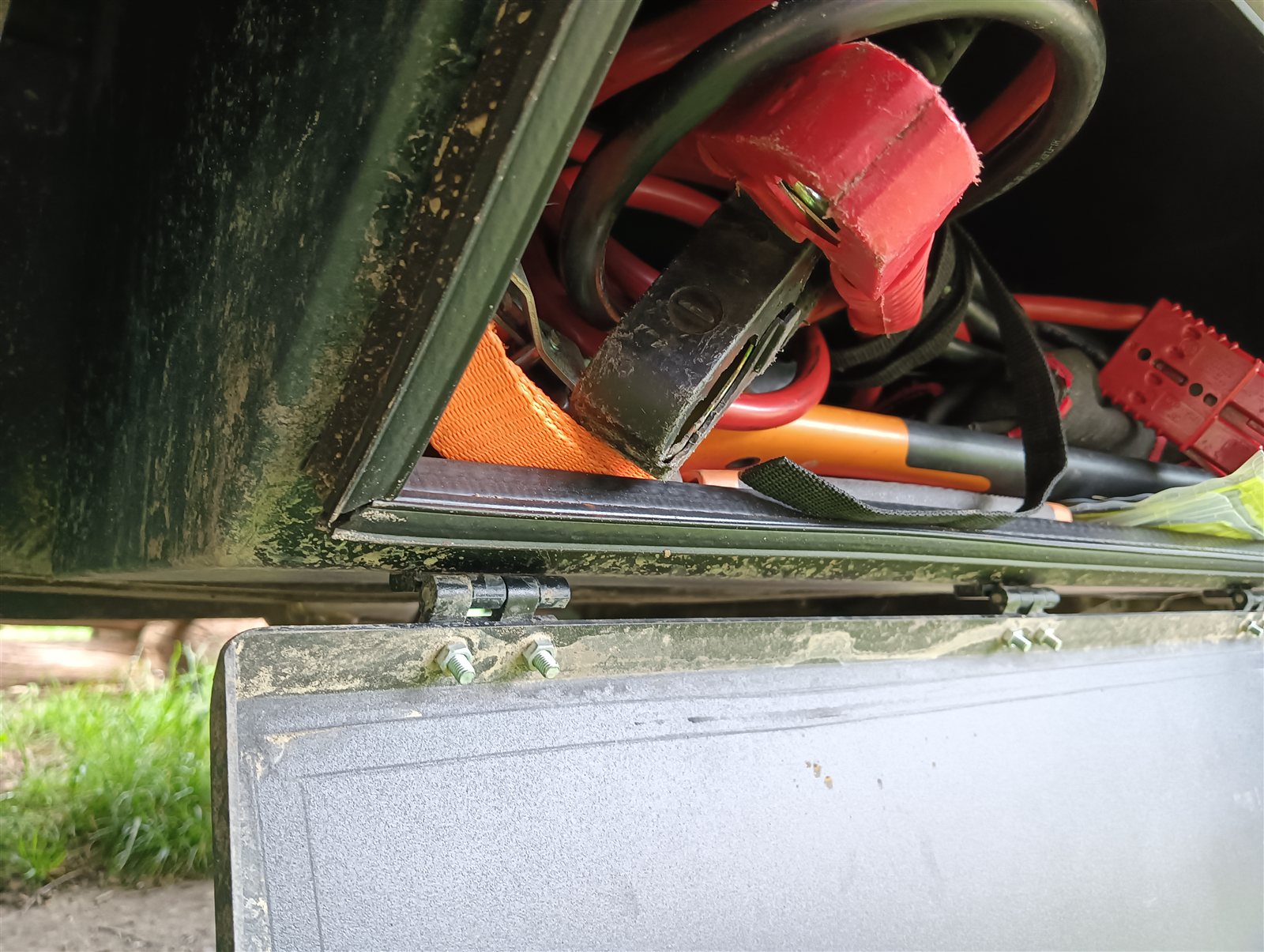 Chassis storage box filled with jumper cables, lashing straps and recovery gear